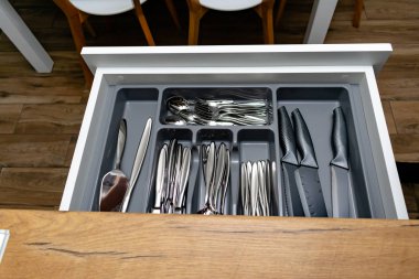 Mutfaktaki siyah kabın içindeki parlak çatal bıçak seti.  