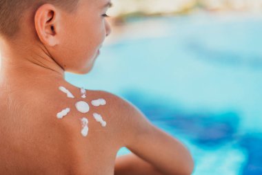 Yüzme havuzunda omzunda güneş kremi olan çocuğun arka görünümü