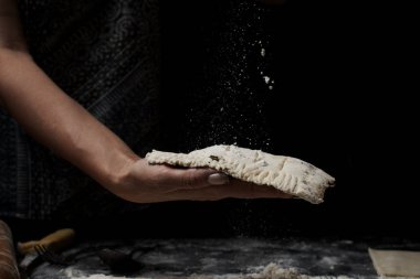 Siyah arka planda taze ev yapımı hamur hazırlayan bir kadın.