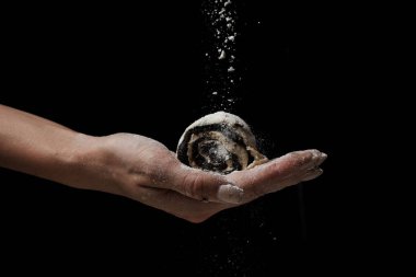 Siyah arka planda haşhaşlı çöreği tutan kadının kısmi görüntüsü