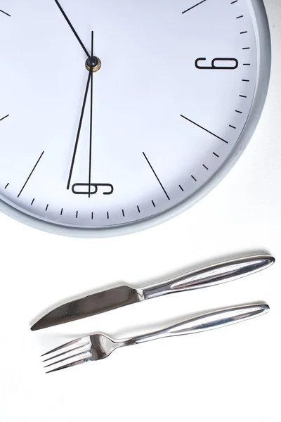 top view of round clock and fork with knife on white background