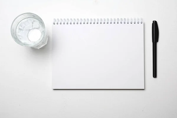 top view of blank notebook, glass of water and pen on white background