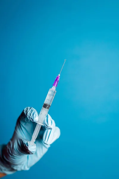 Cropped shot of doctor in glove holding syringe with vaccination on blue background. Syringe with injection solution. Liquid medication or drug
