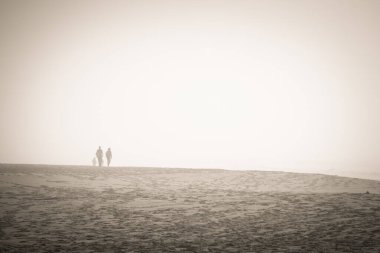 Sisli bir günde çölde dört kişi kumda yürüyor. Güneş parlıyor ama rüzgar soğuk esiyor.