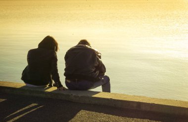 Güneş ışığında deniz kenarında oturan bir çiftin silueti.