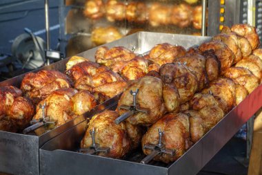 Pazar günü açık hava pazarında ızgara et pişirmek ve ızgara yapmak için dönen tükürüğüyle büyük bir kızartma serisinde kızarmış tavuk.