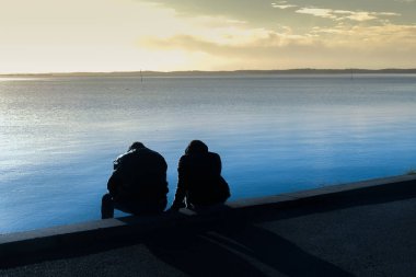 Deniz kenarında oturan heteroseksüel bir çiftin silueti.