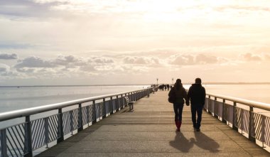 El ele tutuşan bir çiftin silueti, iskelede yürüyor, denize doğru, akşam ışığı sızıntısı gün batımı