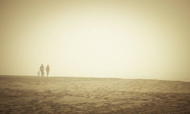 Sisli bir günde çölde dört kişi kumda yürüyor. Güneş parlıyor ama rüzgar soğuk esiyor.