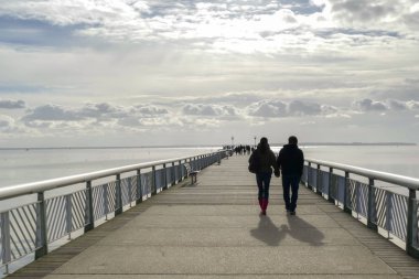 El ele tutuşan bir çiftin silueti, iskelede yürüyor, denize doğru.