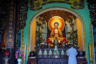 Monk praying in a pagoda with Buddha main statue and several jade sculptures of buddhas.