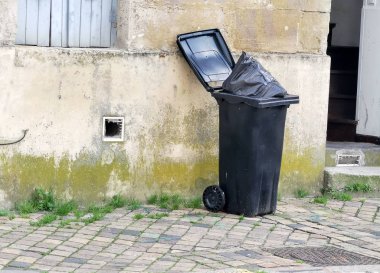 Ön kapı açık ve koyu gri çöp tenekesi çöp ve plastik torbayla dolu.