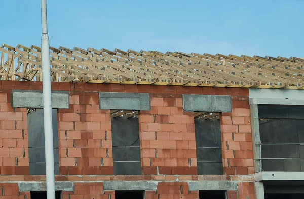 Unfinished brick house, building under construction and wooden roof frame