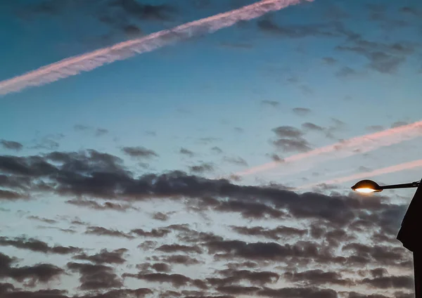 View of house next to a street light against dark sky with clouds, airplane traces, jet trail