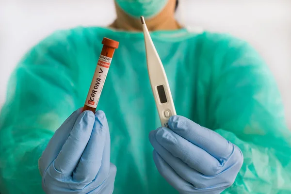 Doktorun elinde bir termometre ve üzerinde kan olan bir test tüpü var.
