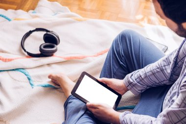 Çocuk tablet ve müzik kulaklıklarıyla odasında yerde oturuyor.