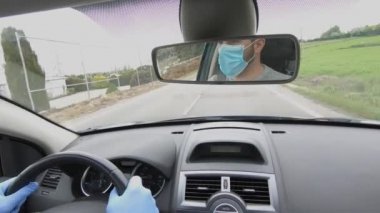 Çocuk dikiz aynasından görülen eldiven ve maskeyle araba kullanıyor.