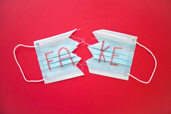 torn and sewn doctor mask with the word fake stamped on red background