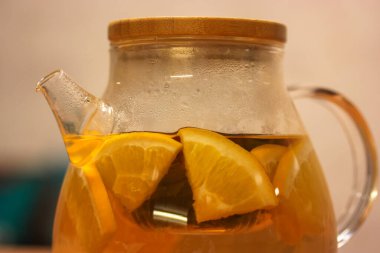 Şeffaf cam su ısıtıcısı ve ev yapımı taze meyveli limonata: portakal, limon, elma. Sonbaharda ya da kışın ısınmak için lezzetli ve sağlıklı içecekler..
