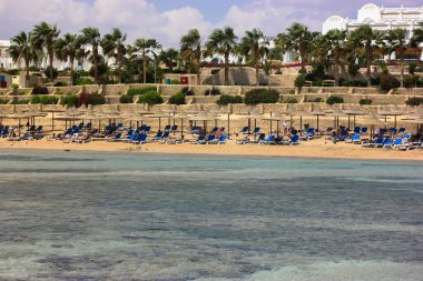 Lüks tatil köyü: güneşten korunmak için sahil ve saman şemsiyeler, deniz kenarında tembel yaz tatili, güneşli güzel bir gün..