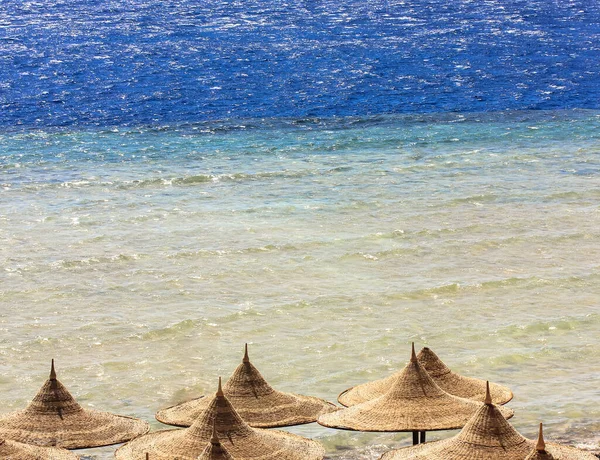 Yaz tatilinde sahilde saman güneş şemsiyeleri ve dalgaların ışıltısı..