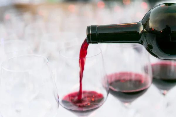 Pouring red wine from a dark green bottle in wine glass close up white background — Stock Photo, Image