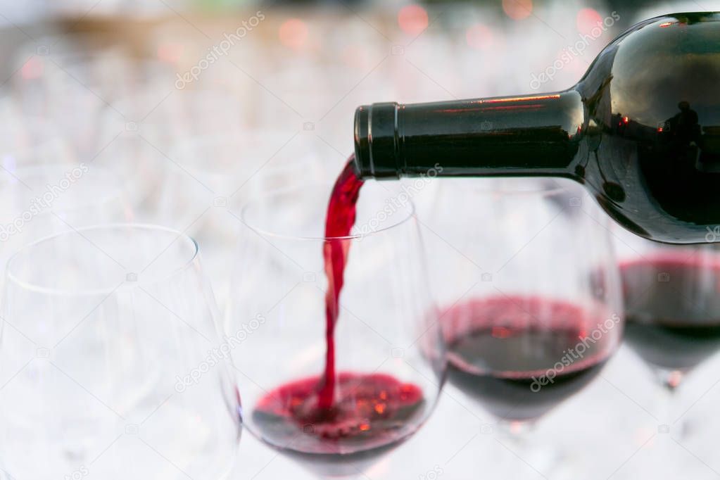 pouring red wine from a dark green bottle in wine glass close up white background