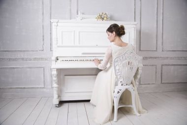 geriye doğru oturma ve piyano beyaz gelinlik içinde genç gelin 