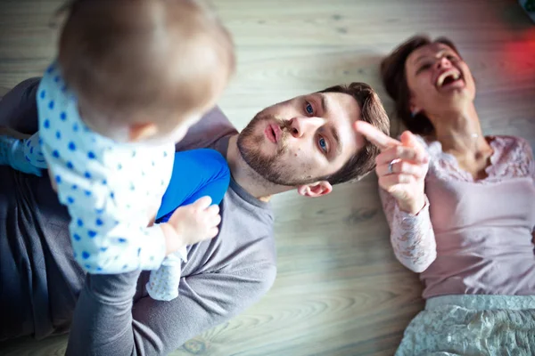 Padres jóvenes juegan con su hija pequeña en el suelo. Mamá se ríe . —  Fotos de Stock