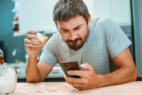 Sakallı sarhoş bir adam cep telefonunun ekranına bakıyor.