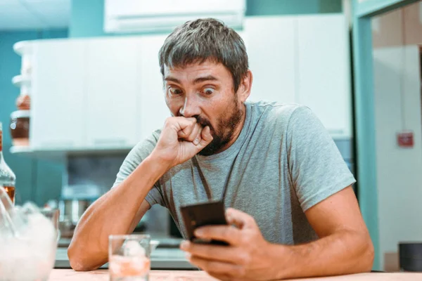 Homem bêbado com barba com medo olha para a tela de um telefone celular Fotografia De Stock