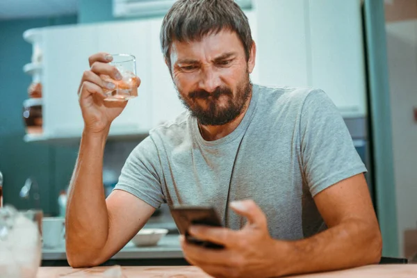 Un homme ivre avec une barbe regarde l'écran d'un téléphone portable Images De Stock Libres De Droits