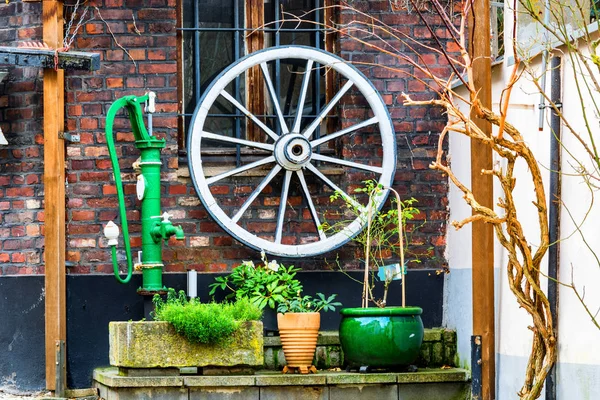 Wooden wagon wheel, water pump on a house wall. — Stock Photo, Image