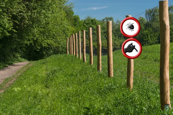 Due segnali di avvertimento rossi rotondi su un palo di recinzione di fronte a un verde — Foto Stock