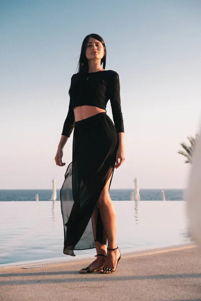 Gün batımında havuz kenarında yürüyen genç ve güzel bir kadın. 