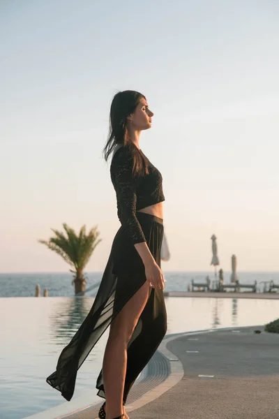 Genç moda güzeli kadın gün batımında sahilde yürüyor.