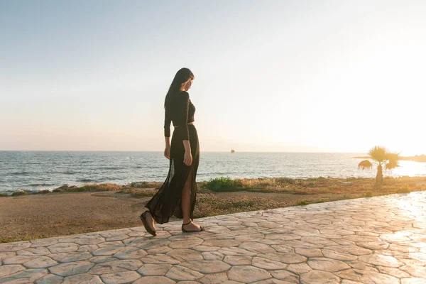 Genç moda güzeli kadın gün batımında sahilde yürüyor.