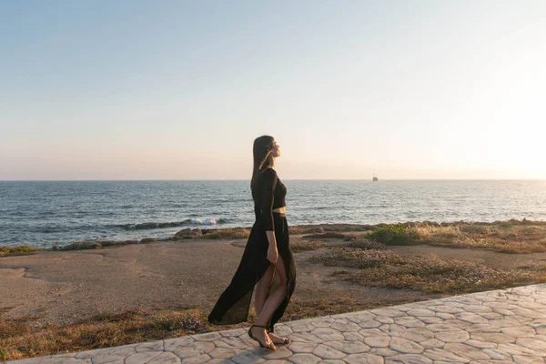 Genç moda güzeli kadın gün batımında sahilde yürüyor.