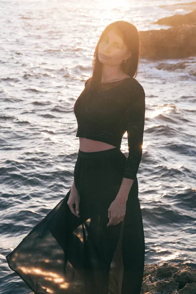 Genç moda güzeli kadın gün batımında sahilde yürüyor.