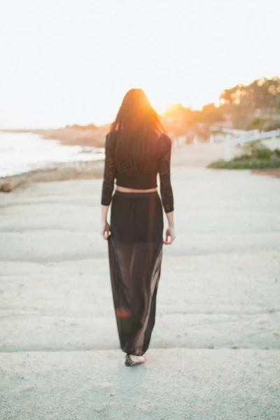 Genç moda güzeli kadın gün batımında sahilde yürüyor.