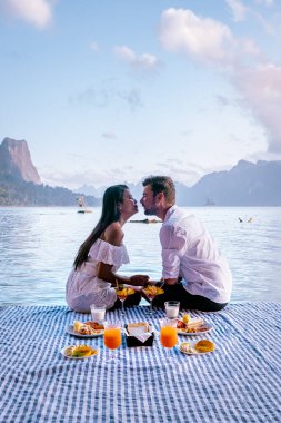 Khao Sok Tayland, Tayland 'daki Khao Sok Ulusal Parkı' nda yüzen bungalovun önünde kahvaltı yapan çift.