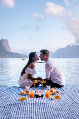 Khao Sok Tayland, Tayland 'daki Khao Sok Ulusal Parkı' nda yüzen bungalovun önünde kahvaltı yapan çift.