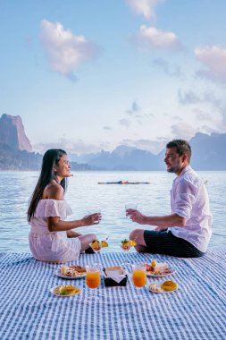 Khao Sok Tayland, Tayland 'daki Khao Sok Ulusal Parkı' nda yüzen ahşap bungalovun önünde kahvaltı yapan çift.