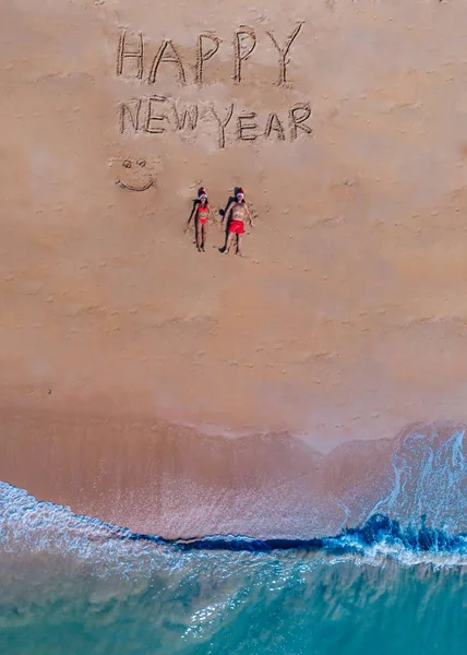 Happy new year sign on the beach with couple in the sand and chritmas hat in Thailand on the beach — Stock Photo, Image