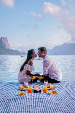 Khao Sok Tayland, Tayland 'daki Khao Sok Ulusal Parkı' nda yüzen ahşap bungalovun önünde kahvaltı yapan çift.