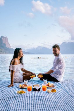 Khao Sok Tayland, Tayland 'daki Khao Sok Ulusal Parkı' nda yüzen ahşap bungalovun önünde kahvaltı yapan çift.