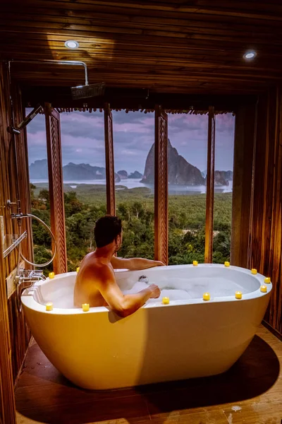 young men in Bath tub with a look over the bay of Phangnga bay, Luxury wooden bathroom during sunset Thailand Asia