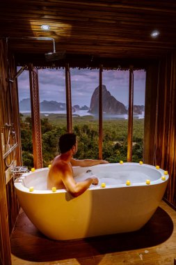young men in Bath tub with a look over the bay of Phangnga bay, Luxury wooden bathroom during sunset Thailand Asia