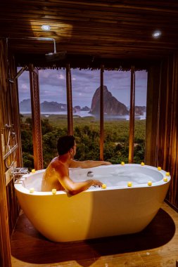 young men in Bath tub with a look over the bay of Phangnga bay, Luxury wooden bathroom during sunset Thailand Asia