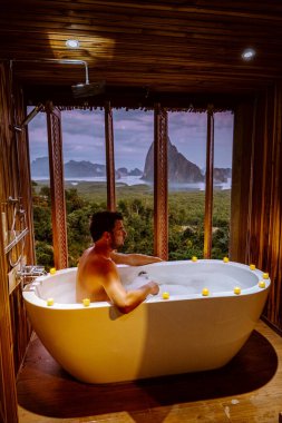 young men in Bath tub with a look over the bay of Phangnga bay, Luxury wooden bathroom during sunset Thailand Asia